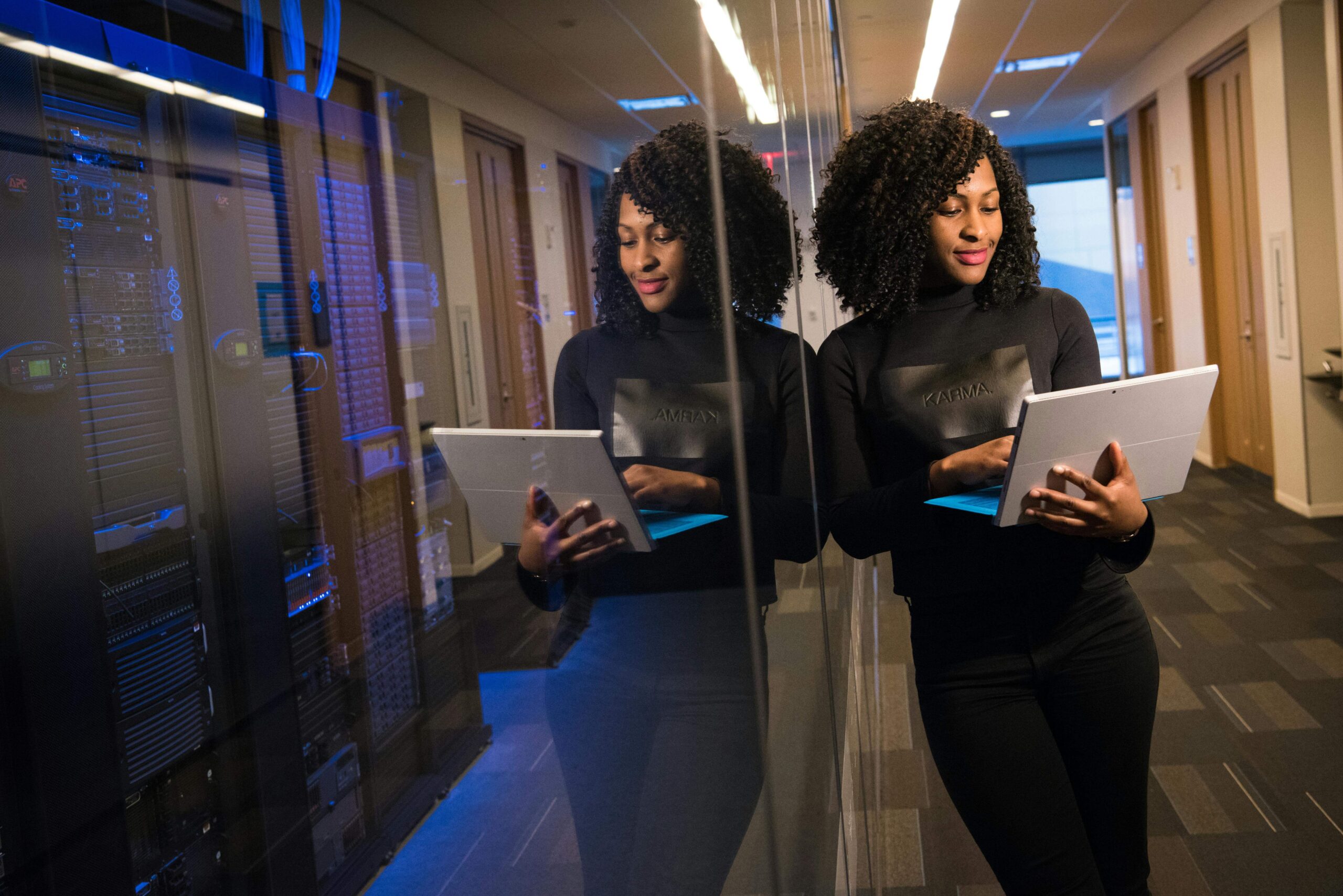 Woman leaning against a glass wall, looking at a laptop with a proud expression